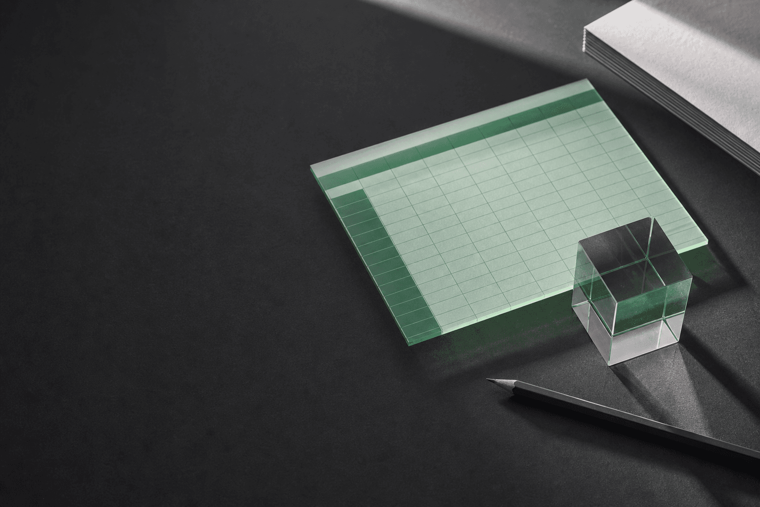 A translucent spreadsheet grid, glass prism, and pencil on a dark work surface